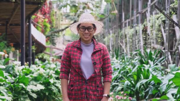 正在微笑的园艺师女人站在温室里的花卉上 在花园工作的年轻女企业家 小企业主的创业 — 图库视频影像