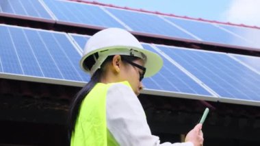 Kasklı ve üniformalı kadın elektrik mühendisi güneş panellerini incelemek için akıllı telefon kullanıyor. Güneş pili istasyonundaki kadın teknisyen. Alternatif enerji kavramı