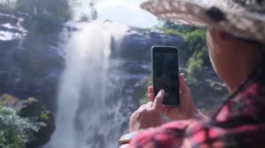 Hasır şapkalı ve kırmızı ekose gömlekli mutlu hippi kadın Chiang Mai kuzey Tayland 'daki Doi Inthanon Ulusal Parkı' ndaki Wachirathan şelalesinde doğanın tadını çıkarıyor. Tayland Seyahat Konsepti