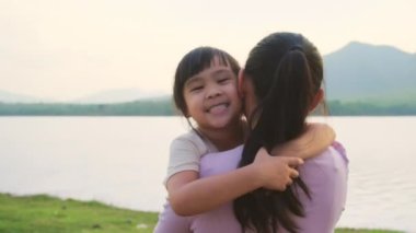 Anne, gün batımında göl kenarında yürüyen tatlı bir kız çocuğu tutuyor. Heyecanlı kız dışarıda annesiyle oynarken güler. Anne kızını kucaklıyor..
