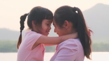 Anne, gün batımında göl kenarında yürüyen tatlı bir kız çocuğu tutuyor. Heyecanlı kız dışarıda annesiyle oynarken güler. Anne kızını kucaklıyor..