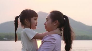 Anne, gün batımında göl kenarında yürüyen tatlı bir kız çocuğu tutuyor. Heyecanlı kız dışarıda annesiyle oynarken güler. Anne kızını kucaklıyor..