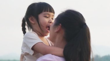 Anne, gün batımında göl kenarında yürüyen tatlı bir kız çocuğu tutuyor. Heyecanlı kız dışarıda annesiyle oynarken güler. Anne kızını kucaklıyor..