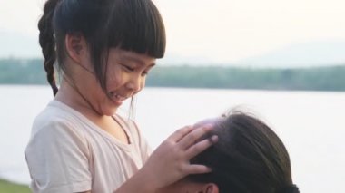 Anne, gün batımında göl kenarında yürüyen tatlı bir kız çocuğu tutuyor. Heyecanlı kız dışarıda annesiyle oynarken güler. Anne kızını kucaklıyor..