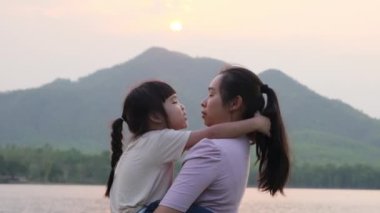 Anne, gün batımında göl kenarında yürüyen tatlı bir kız çocuğu tutuyor. Heyecanlı kız dışarıda annesiyle oynarken güler. Anne kızını kucaklıyor..