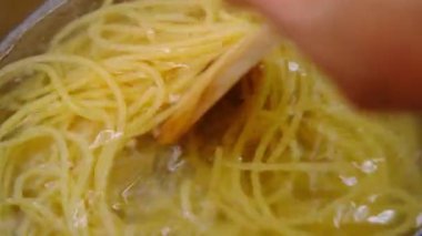 Fırının üstünde, ahşap bir kepçeyle el çırpılmış makarna. Evde yemek pişirmek. Ev yapımı Carbonara spagettisi hazırlığı.