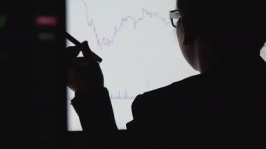 İş kadını, hisse senedi veri tablosuna bakıyor. Belgeye not alıyor ve bilgisayar borsası verilerini kontrol ediyor. Bu sırada da geceleri piyasadaki oyun hisselerinin analizini yapıyor..