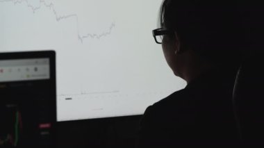 İş kadını, hisse senedi veri tablosuna bakıyor. Belgeye not alıyor ve bilgisayar borsası verilerini kontrol ediyor. Bu sırada da geceleri piyasadaki oyun hisselerinin analizini yapıyor..