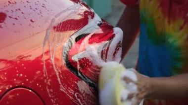 Close-up of a woman's hand washing a car with sponge and soap on the car wash. Manual car wash with white soap. Car wash service concept.