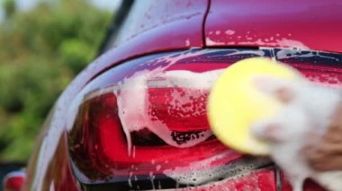 Close-up of a woman's hand washing a car with sponge and soap on the car wash. Manual car wash with white soap. Car wash service concept.
