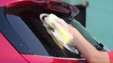 Close-up of a woman's hand washing a car with sponge and soap on the car wash. Manual car wash with white soap. Car wash service concept.