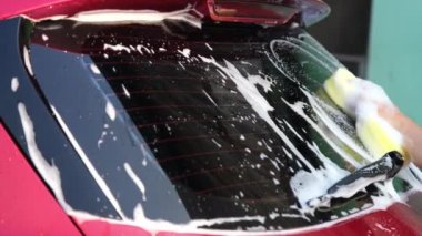 Close-up of a woman's hand washing a car with sponge and soap on the car wash. Manual car wash with white soap. Car wash service concept.