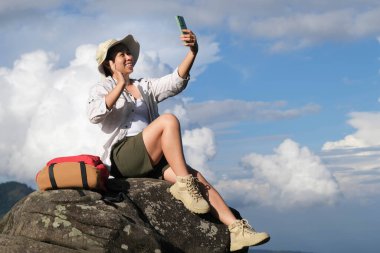 Uçurumda oturan ve cep telefonu kullanan mutlu bir kadın. Genç bayan yürüyüşçü akıllı telefon dağ zirvesi kullanır. Dağın tepesinde akıllı telefonuyla selfie çeken bir kadın..