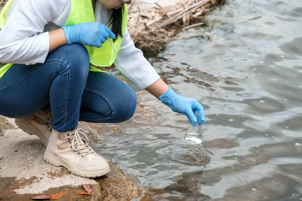 Eldivendeki kadın çevreci eller enfeksiyonları araştırmak ve test etmek için nehirden su örnekleri topluyor. Su ve ekoloji kavramı