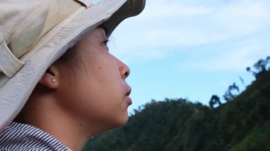 Sırt çantalı ve şapkalı mutlu bir kadın yolcunun yan portresi bir dağda durup doğanın tadını çıkarıyor ve gökyüzüne bakıyor. Seyahat ve Özgürlük kavramı