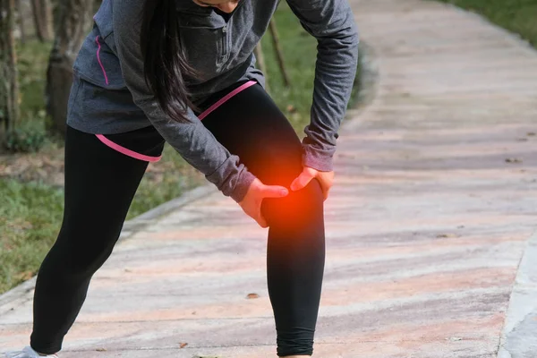 Female runner touches her knee in pain while jogging in a park. Runner sport knee injury.