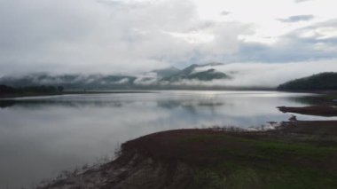 Aerial view from drone, beautiful view of morning mist covering forests and mountains with calm rivers(Lam Taphen Reservoir), Kanchanaburi Province, Thailand.