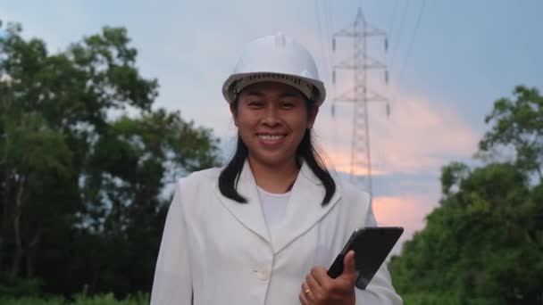 Азиатская Женщина Электрик Держит Планшет Улыбается Фоне Высокого Напряжения Полюса — стоковое видео