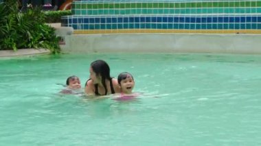 Asyalı aile havuzda eğleniyor, havuz başında otururken bacaklarıyla su sıçratıyorlar. Mutlu aile yaz tatilini birlikte geçirdi..