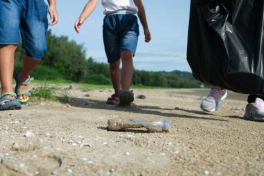 Plajı temizleyen eldivenli anne ve kızları. Bir grup genç gönüllü doğayı temiz tutmaya ve kumlu bir sahilden çöpleri toplamaya yardım ediyor. Dünya Günü konsepti