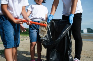 Plajı temizleyen eldivenli anne ve kızları. Bir grup genç gönüllü doğayı temiz tutmaya ve kumlu bir sahilden çöpleri toplamaya yardım ediyor. Dünya Günü konsepti