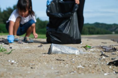 Plajı temizleyen eldivenli anne ve kızları. Bir grup genç gönüllü doğayı temiz tutmaya ve kumlu bir sahilden çöpleri toplamaya yardım ediyor. Dünya Günü konsepti