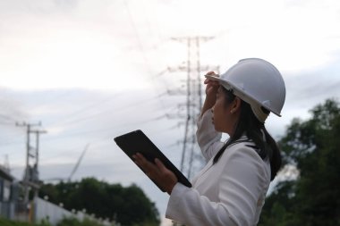 Asyalı kadın elektrik mühendisi yüksek voltaj direğinin yanında dizüstü bilgisayarda çalışıyor. Güç şebekesini inceliyor. Elektrik üretimi için Rüzgar Türbini Mühendisi. yenilenebilir enerji kavramı