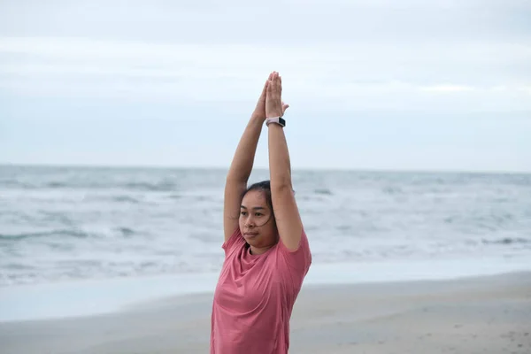 Asian woman practicing yoga at seashore. Young beautiful woman stretching and doing yoga outdoors on blue yoga mat on beach. relaxing in nature