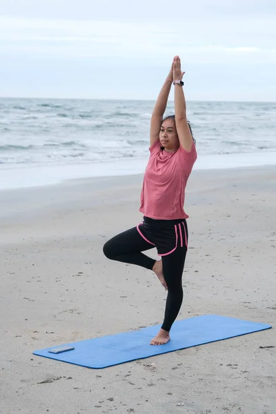 Asian woman practicing yoga at seashore. Young beautiful woman stretching and doing yoga outdoors on blue yoga mat on beach. relaxing in nature