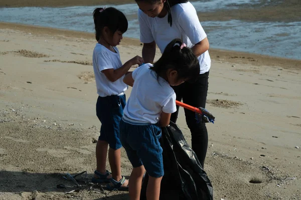 Mother and daughters in gloves cleaning up the beach. Group of young volunteers helping to keep nature clean and picking up the garbage from a sandy shore. Earth day concept