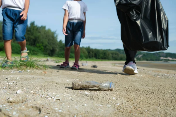 Mother and daughters in gloves cleaning up the beach. Group of young volunteers helping to keep nature clean and picking up the garbage from a sandy shore. Earth day concept