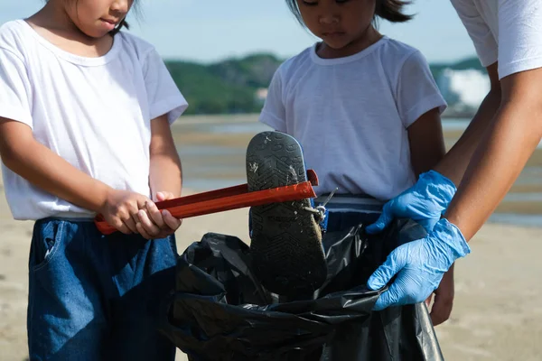 Mother and daughters in gloves cleaning up the beach. Group of young volunteers helping to keep nature clean and picking up the garbage from a sandy shore. Earth day concept