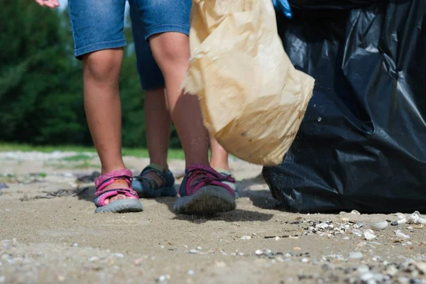 Mother and daughters in gloves cleaning up the beach. Group of young volunteers helping to keep nature clean and picking up the garbage from a sandy shore. Earth day concept