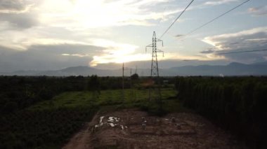 Kırsal kesimde günbatımında gökyüzünde yüksek voltajlı sütunların ve kabloların havadan görüntüsü. Elektrik direklerinin ve kabloların alacakaranlıktaki drone görüntüleri..