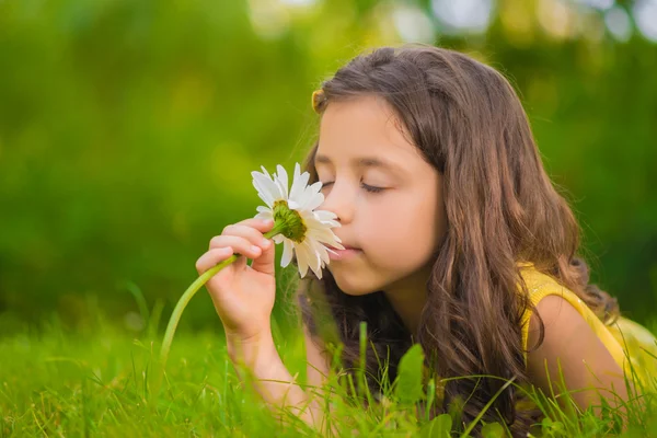 Маленькая девочка лежит в траве и чувствует запах цветка. — стоковое фото