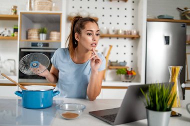 Genç bir kadın laptopta yemek pişirirken yemek tarifleri izliyor..