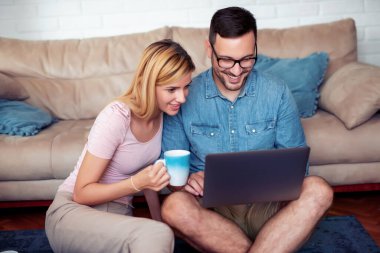 Young couple relaxing at home, surfing on a laptop computer and drinking coffee. 