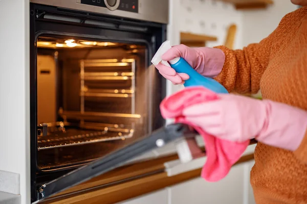 Koruyucu eldivenli kadın fırını temizliyor. Ev işi ve temizlik konsepti. .
