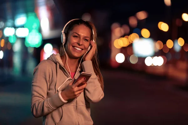 Young woman running at night in the city and listening to music.