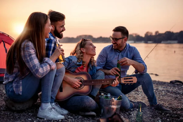 Bir grup genç arkadaş nehrin kenarında oturup gitar çalıyor ve eğleniyorlar..