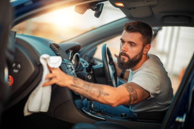 Genç adam arabasını mikrofiber bezle temizliyor..