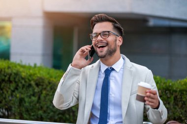 Genç adam iş için akıllı telefon kullanıyor, gitmek için kahve içiyor..