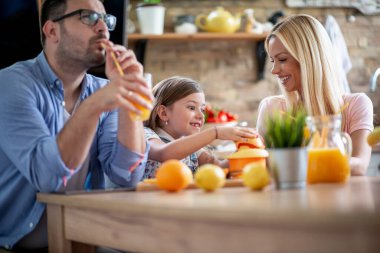 Mother, father and daughter making fresh orange juice at home in the kitchen. Family,happiness and people concept.