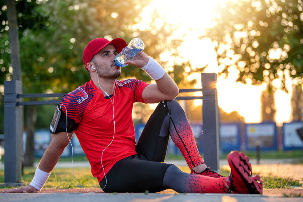 Young man sitting outdoor and drink wather after jogging.