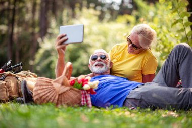 Yaşlı çift parkta tablet kullanarak eğleniyor. Romantik anlar.