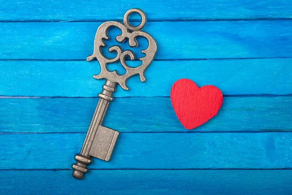 Старый ключ и красное сердце на синем деревянном фоне — стоковое фото