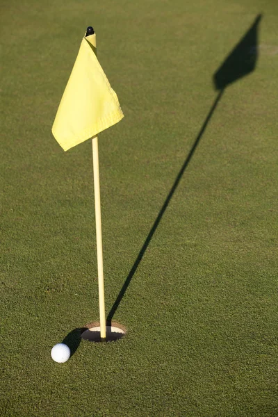 Vit golfbollen nära hål flagga på ett fält — Stockfoto