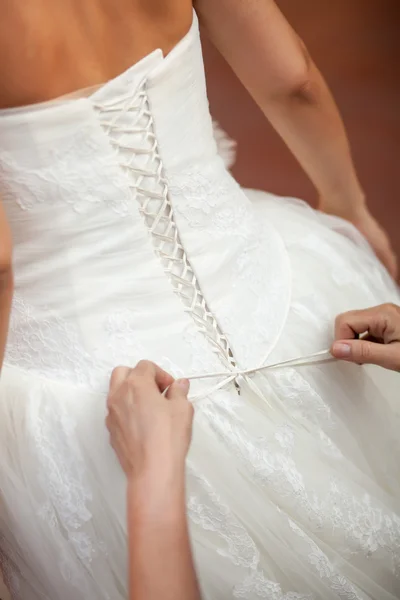 Bruidsmeisje helpen de bruid om haar trouwjurk op. koppelverkoop boog op trouwjurk — Stockfoto