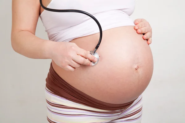 Pregnant woman listening her belly with stethoscope — Stock Photo, Image