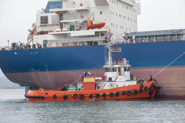 Красный буксир, помогающий огромному кораблю в порту — стоковое фото